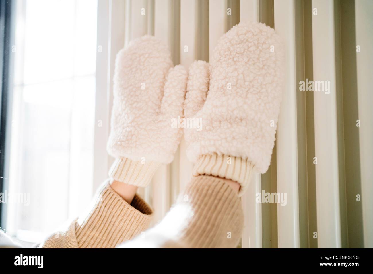 Mani di ragazza adolescente con i mitens che toccano sul riscaldatore del radiatore Foto Stock