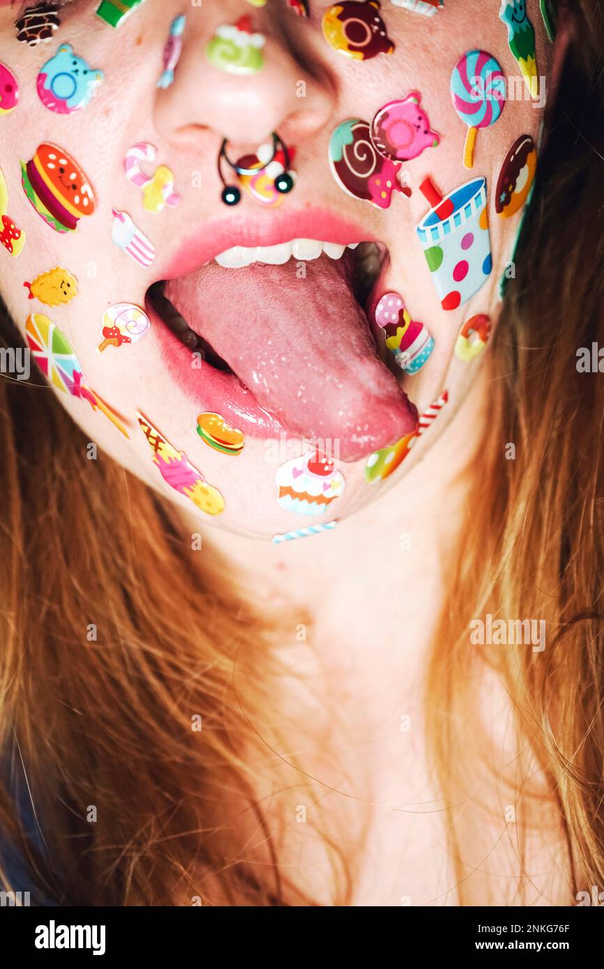 Donna con anello nasale e adesivi sul viso che sporgono dalla lingua Foto Stock