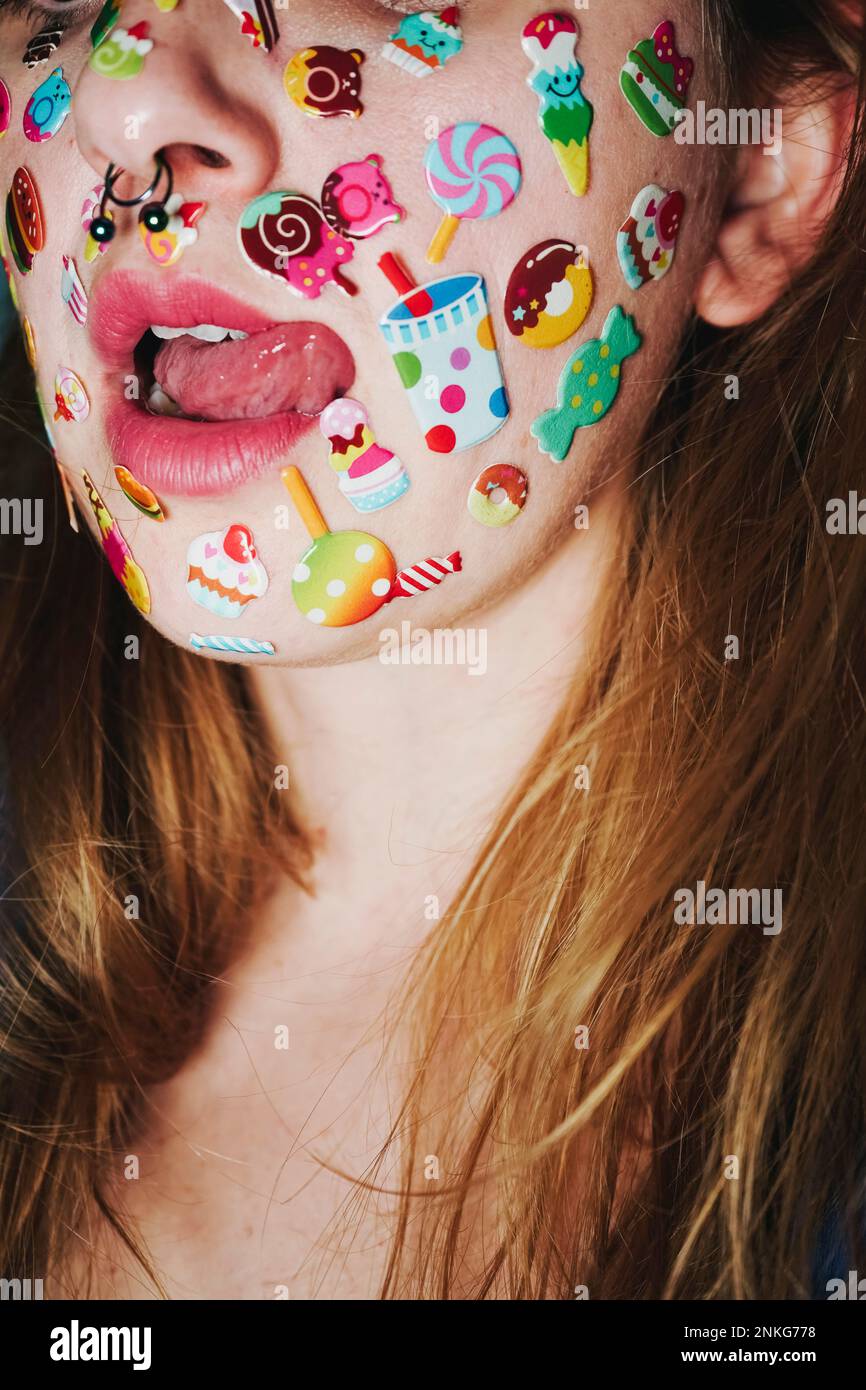 Donna con adesivi sul viso che sporgono dalla lingua Foto Stock
