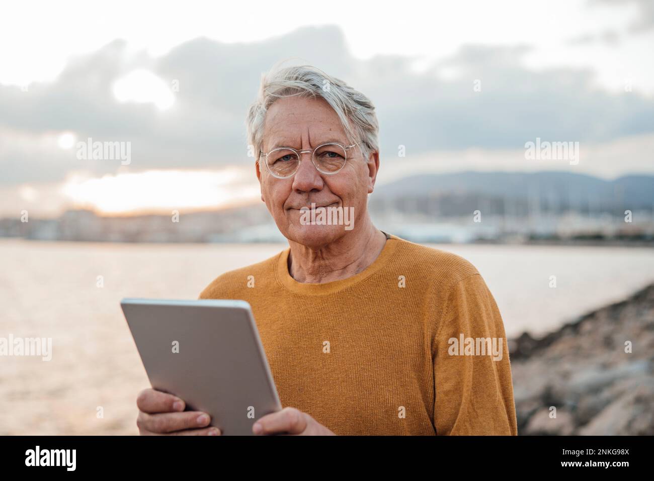 Uomo anziano sorridente in piedi con un tablet Foto Stock