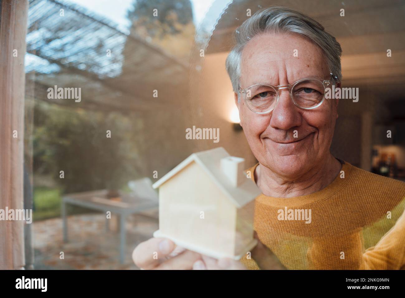 Uomo sorridente con la casa modello vista attraverso il vetro Foto Stock