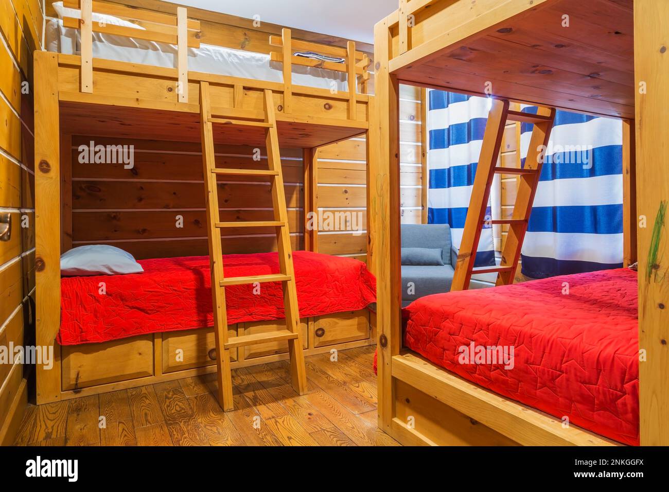 Letti a castello in legno di pino con copriletto rosso in camera da letto per bambini con pavimento in legno duro interno fresato legno di pino bianco orientale e casa con profilo in tronchi piatto. Foto Stock