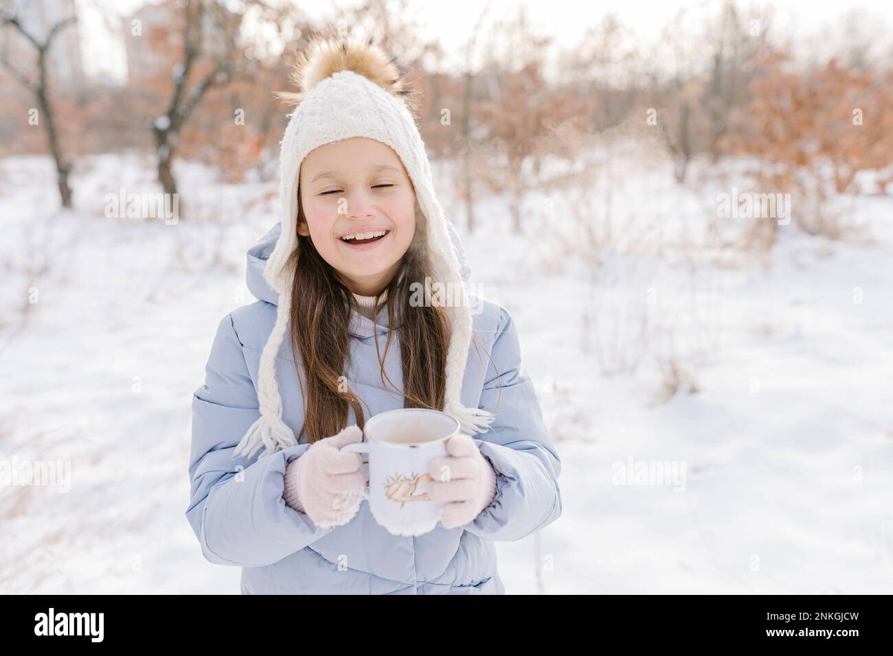 Ragazza felice con tazza di cioccolata calda in piedi nella neve Foto Stock