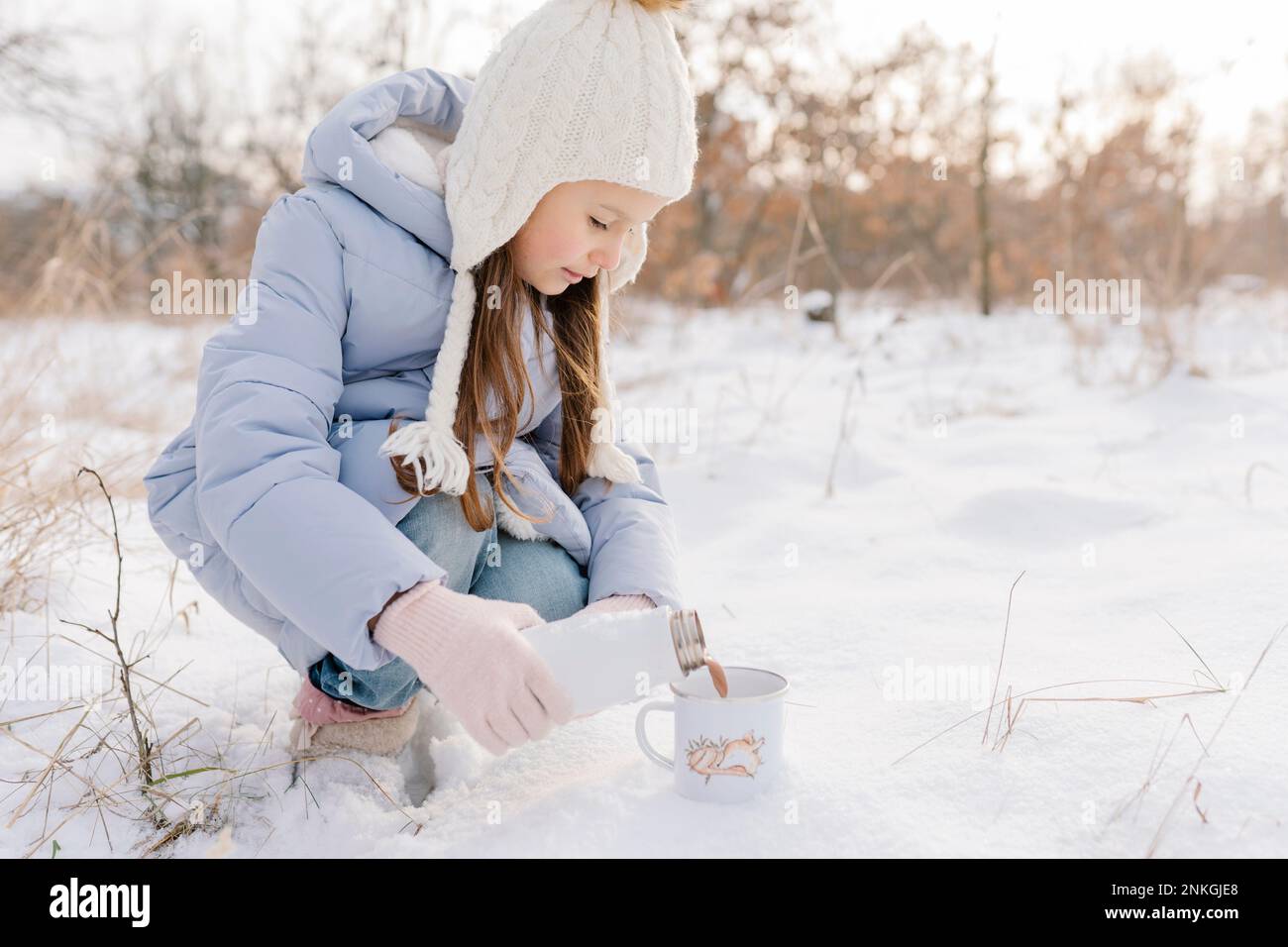 Ragazza che indossa un cappello a maglia che versa cioccolata calda in tazza Foto Stock