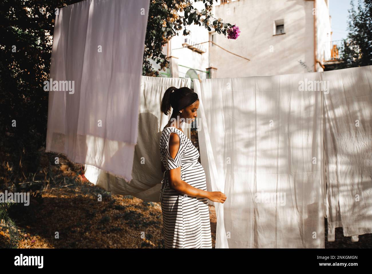 Donna incinta che appende il foglio bianco nel cortile posteriore Foto Stock