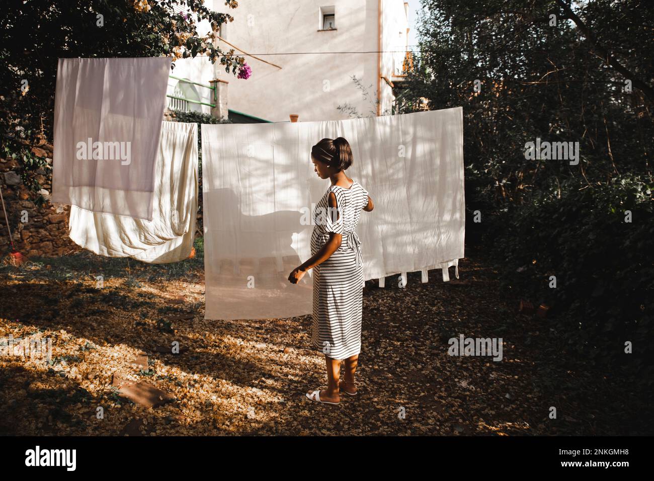 Donna incinta che appende il foglio bianco al cortile nel giardino Foto Stock