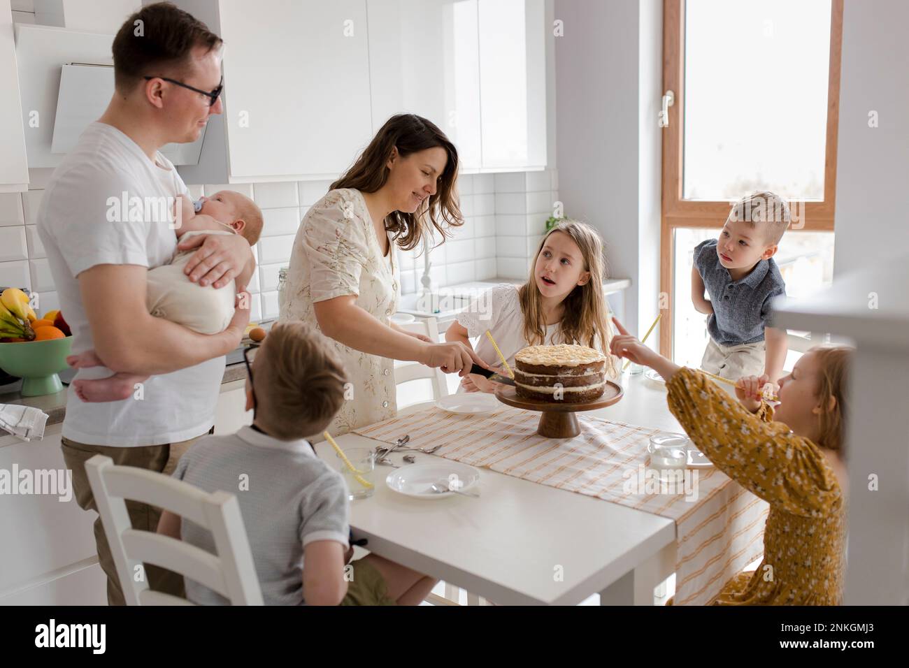 Madre torta di taglio con i bambini seduti al tavolo in cucina Foto Stock