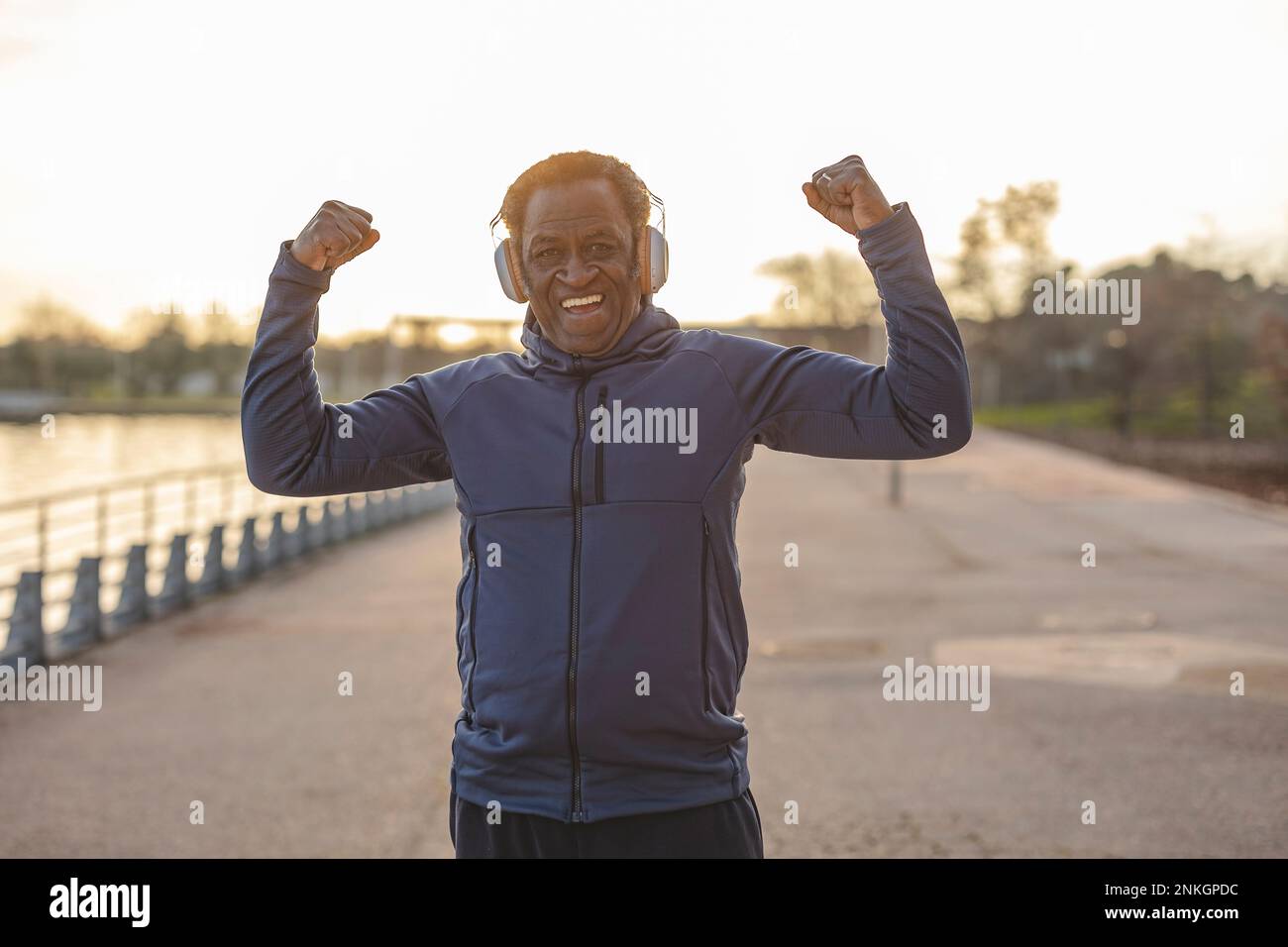 Felice uomo anziano che indossa cuffie che flettono i muscoli sul lungomare Foto Stock