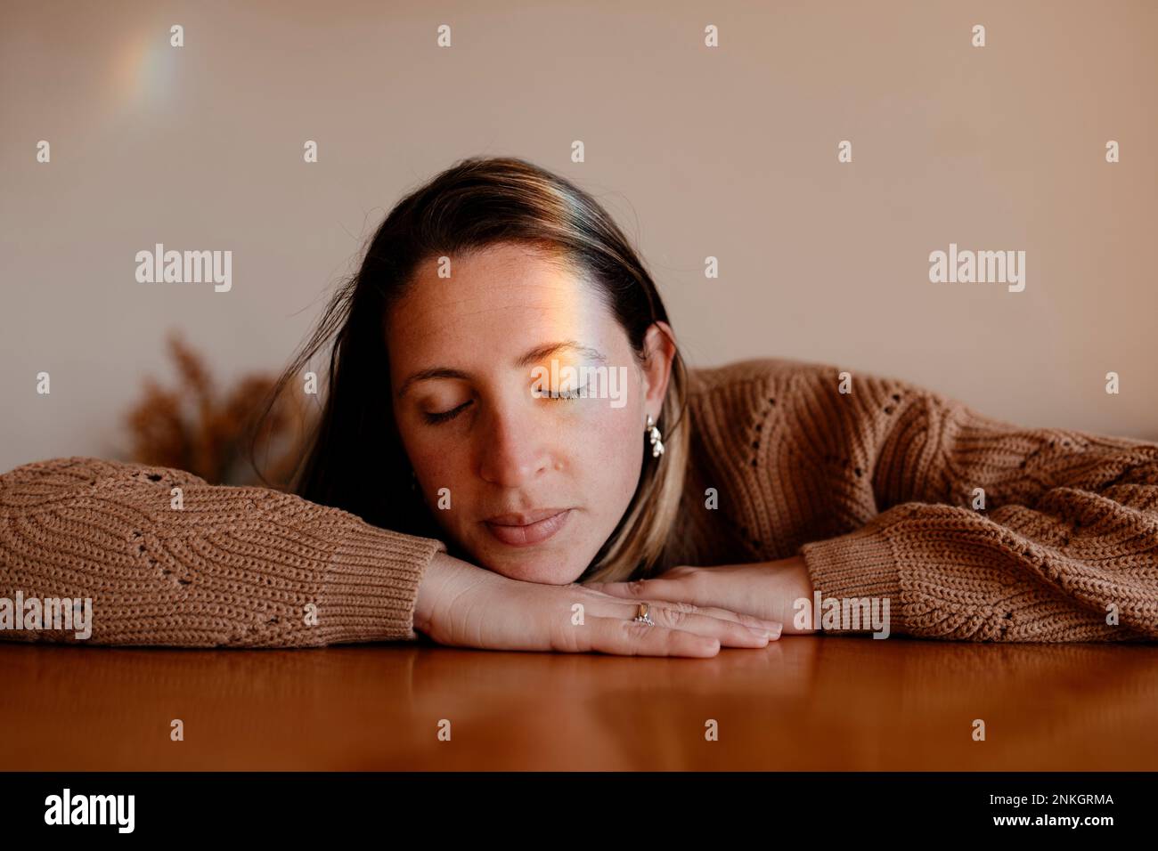Donna con luce arcobaleno sul viso che riposa al tavolo Foto Stock