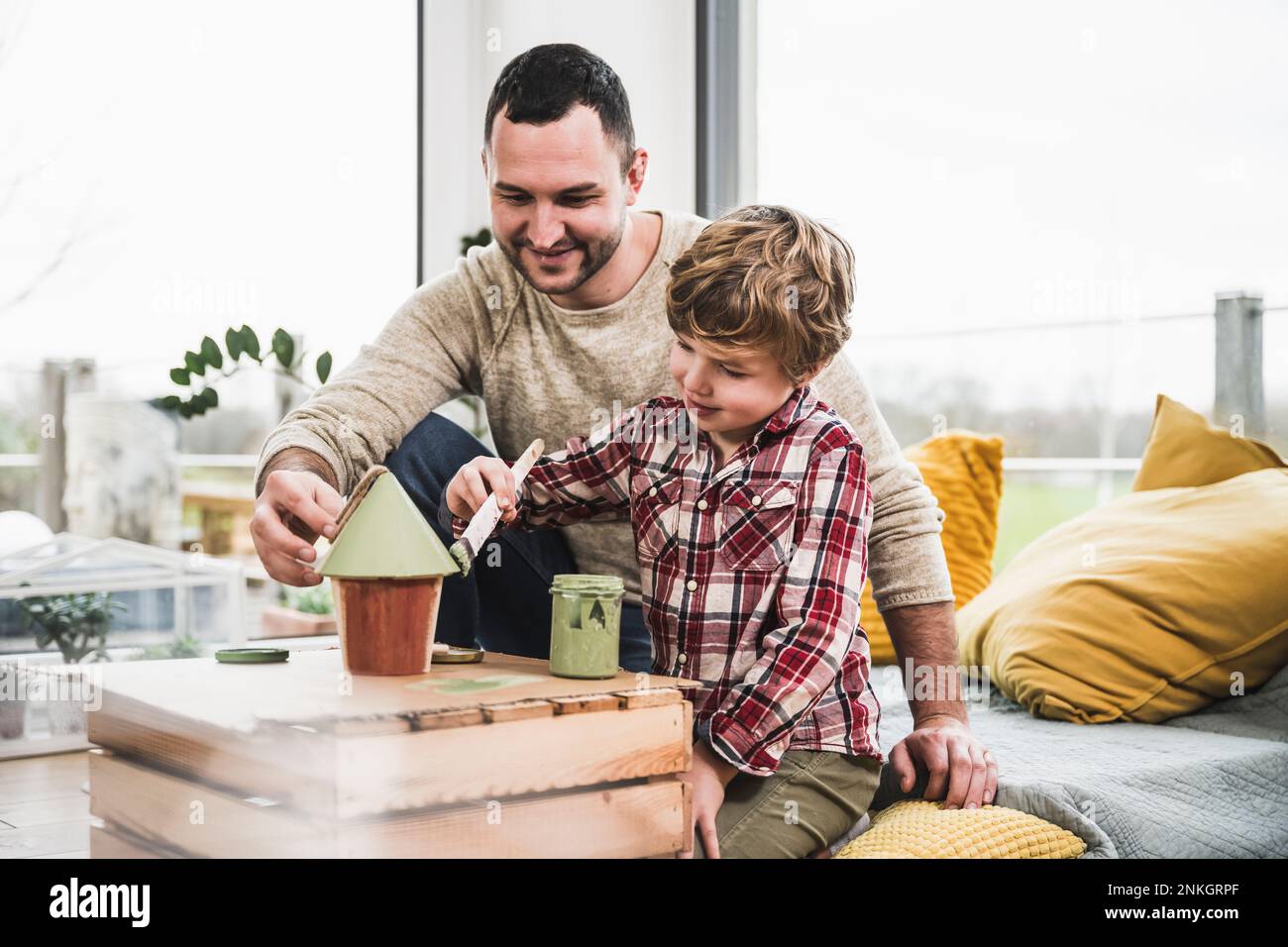 Sorridente figlio dipingendo modello casa da padre a casa Foto Stock