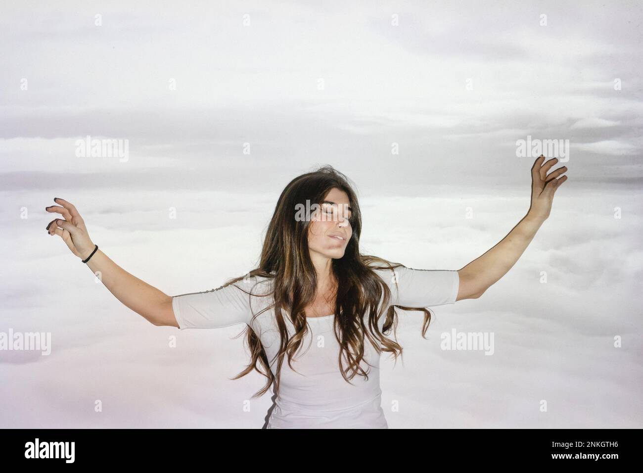 Donna spensierata con le braccia distese sulla proiezione di nuvole sul muro Foto Stock