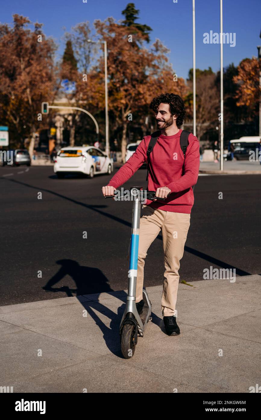 Felice giovane uomo in piedi con lo scooter elettrico a spinta sulla strada Foto Stock