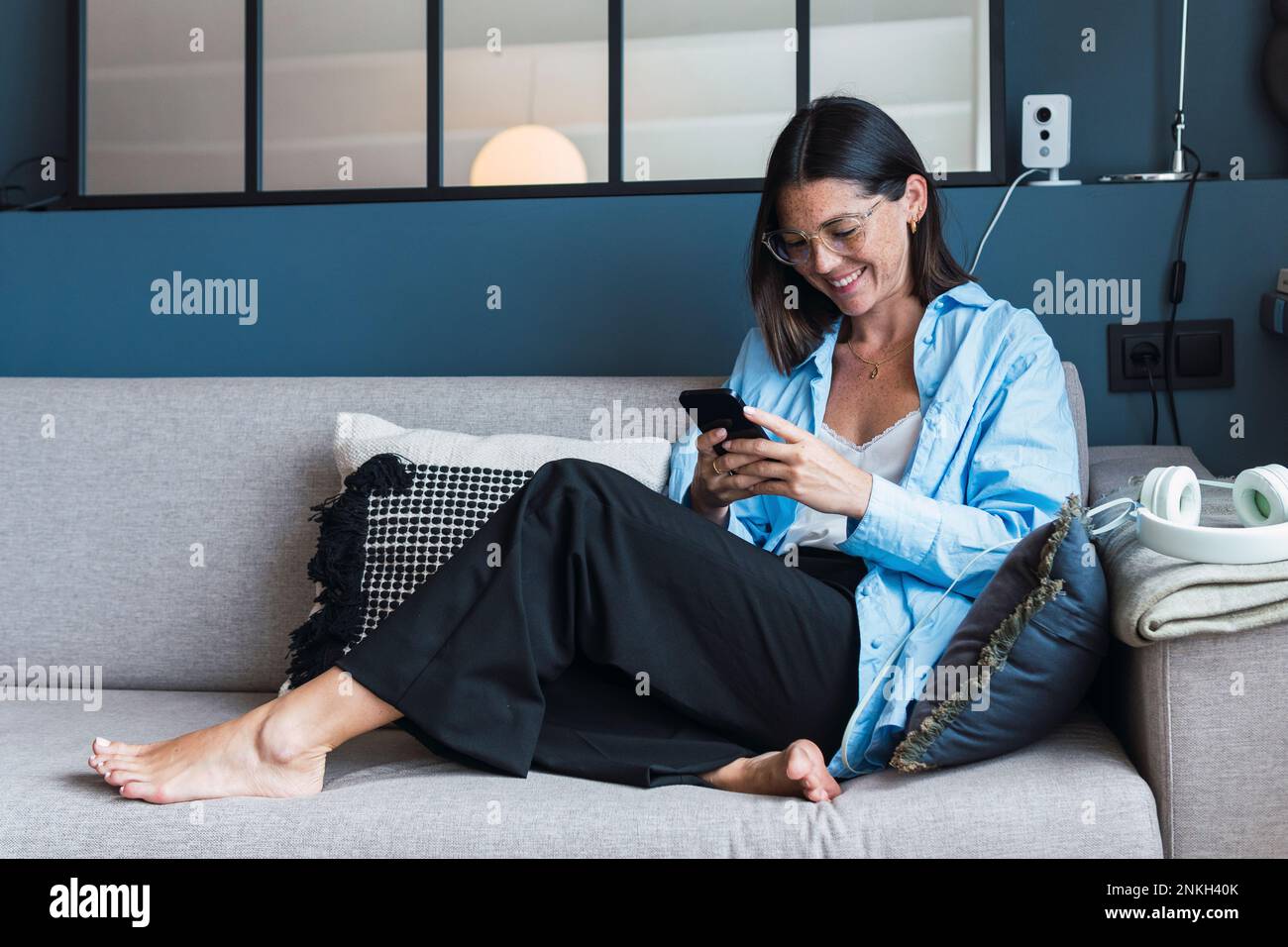 Donna sorridente che usa lo smartphone in salotto Foto Stock