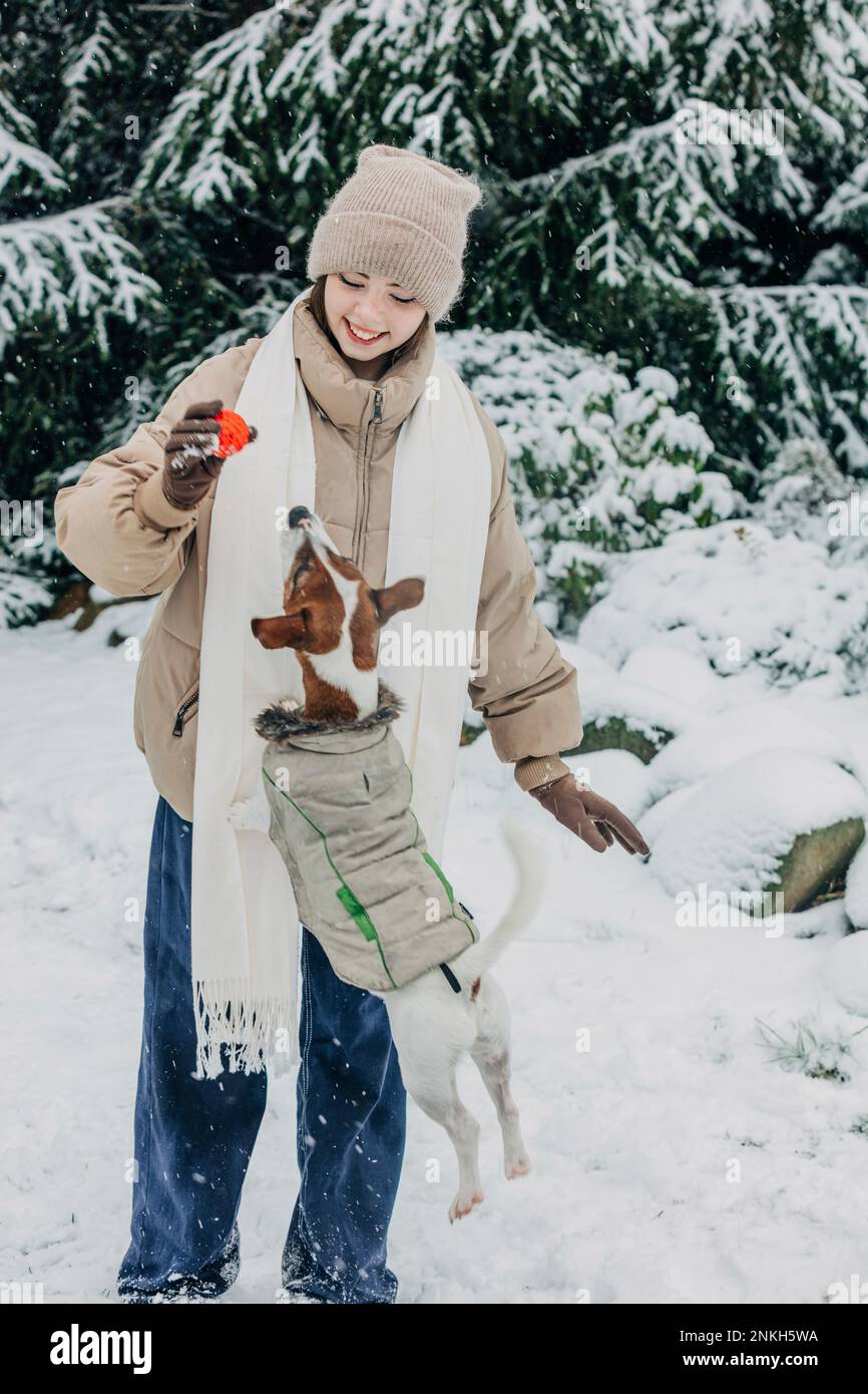 Giovane donna sorridente che gioca con il cane nel parco innevato Foto Stock