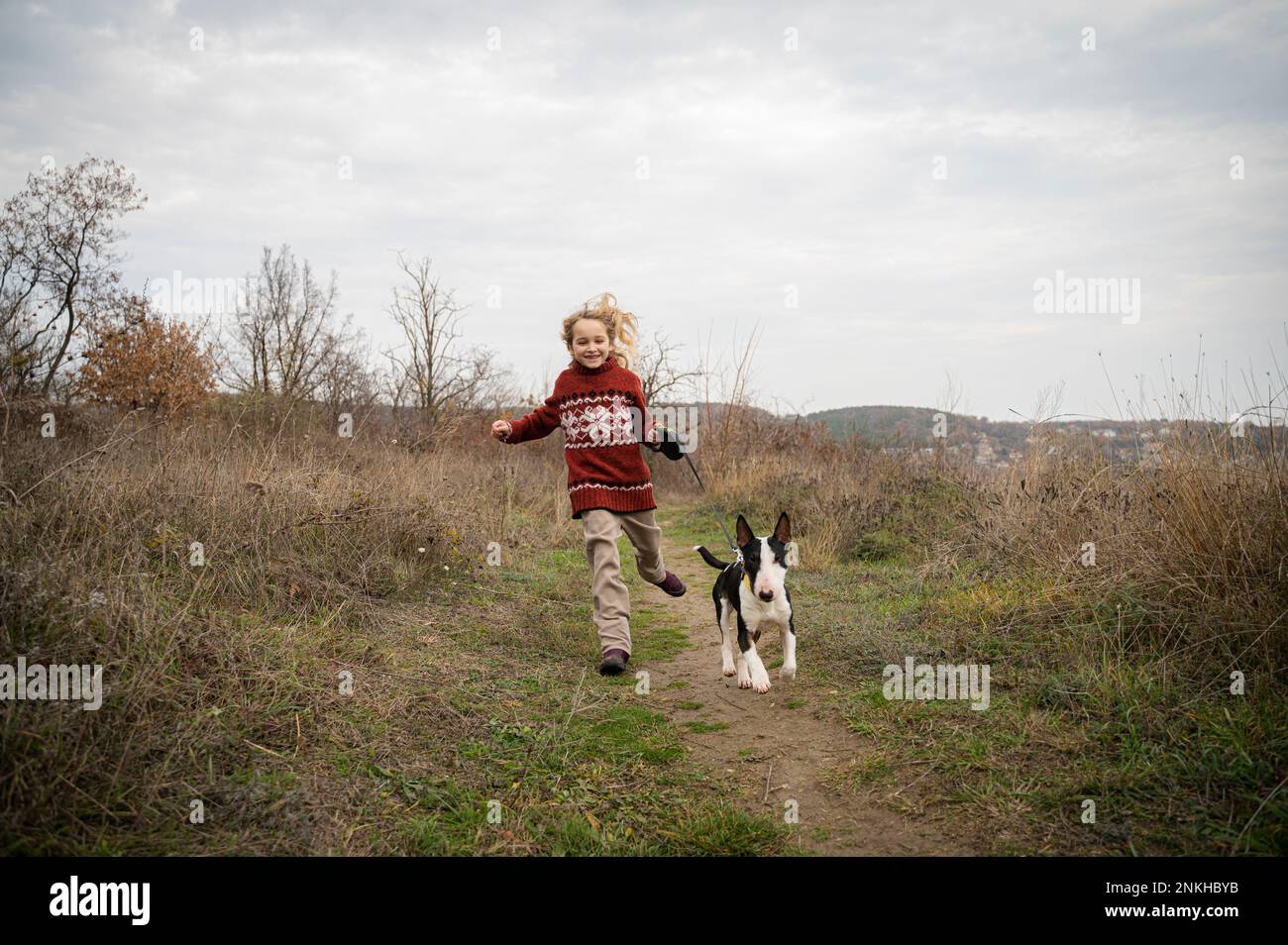 Ragazza sorridente che corre con il cane attraverso l'erba Foto Stock