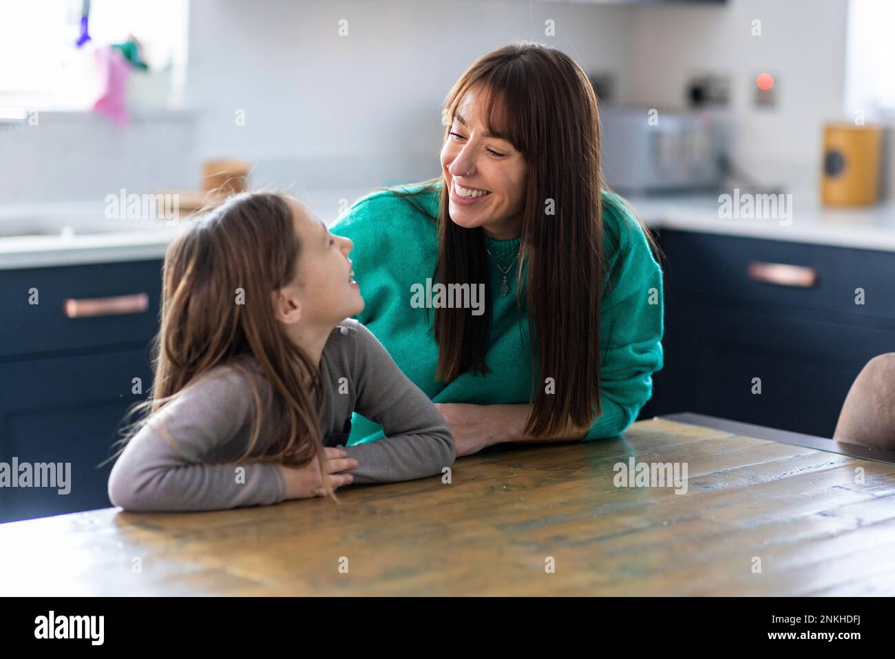 Madre e figlia sorridenti seduti al tavolo in cucina Foto Stock