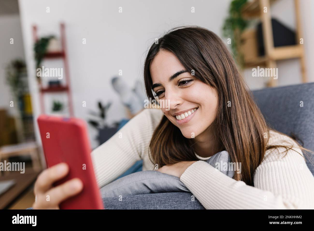 Messaggi di testo per donna felice tramite smartphone in salotto Foto Stock
