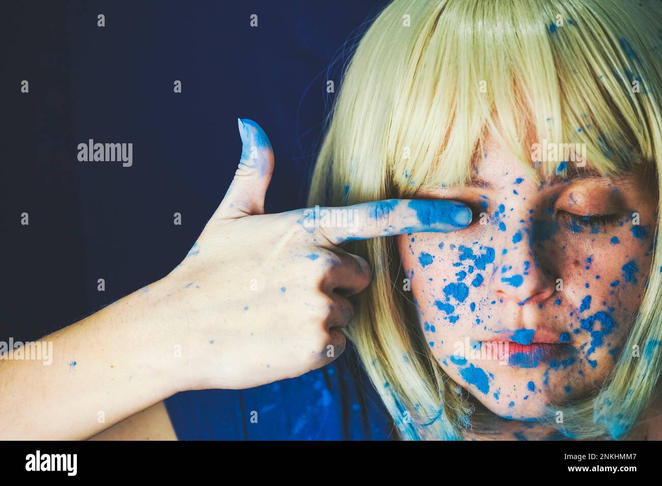 Donna con vernice blu sul viso che tocca l'occhio su sfondo blu Foto Stock