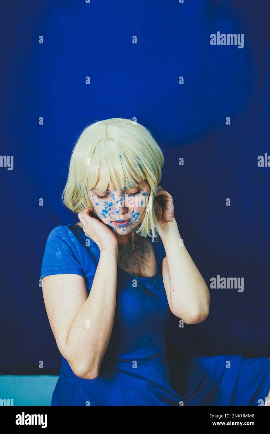 Donna bionda coperta di polvere blu dolore seduto di fronte al muro Foto Stock