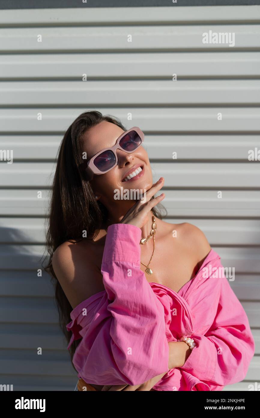 Giovane bella brunetta in una camicia rosa, gioielli da collo, collana, occhiali  da sole alla moda sullo sfondo di un recinto porta garage leggero Foto  stock - Alamy