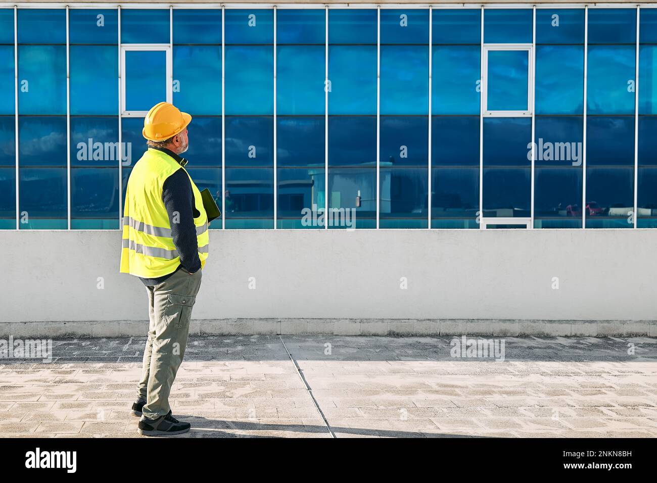 Supervisore al ribasso di mezza età in elmetto e giubbotto di sicurezza con tablet sul sito dell'edificio. L'ingegnere strutturale o architetto monitora l'avanzamento di Foto Stock