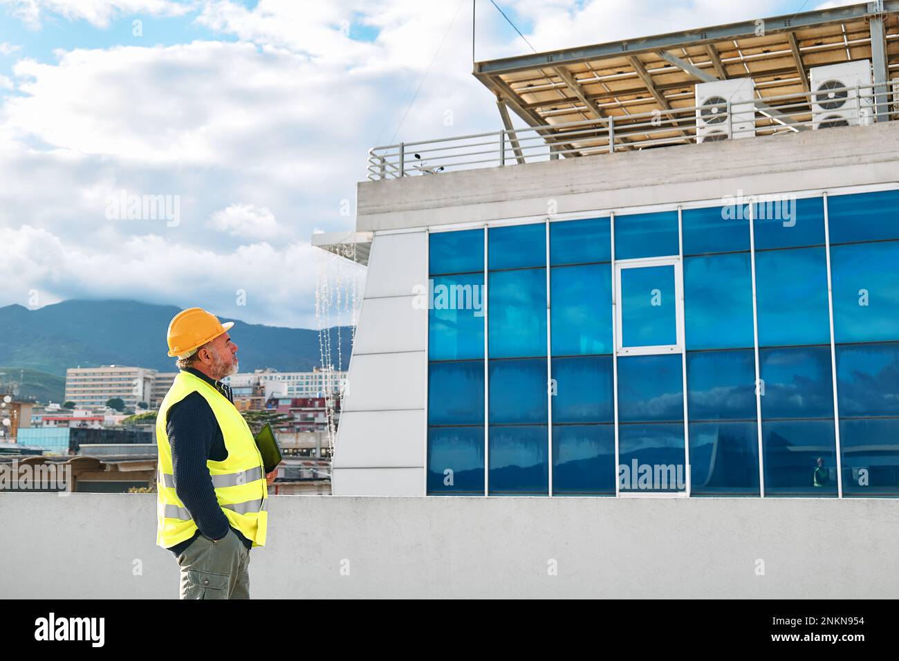 Supervisore al ribasso di mezza età in elmetto e giubbotto di sicurezza con tablet sul sito dell'edificio. L'ingegnere strutturale o architetto monitora l'avanzamento di Foto Stock