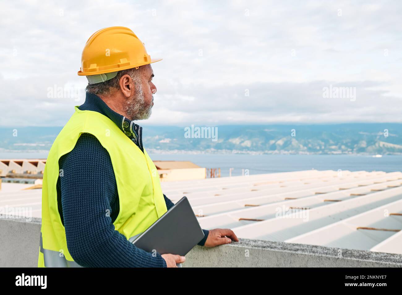 Ritratto del supervisore bearded di mezza età in elmetto e giubbotto di sicurezza con tablet sul sito dell'edificio. L'ingegnere strutturale o architetto monitora il prog Foto Stock