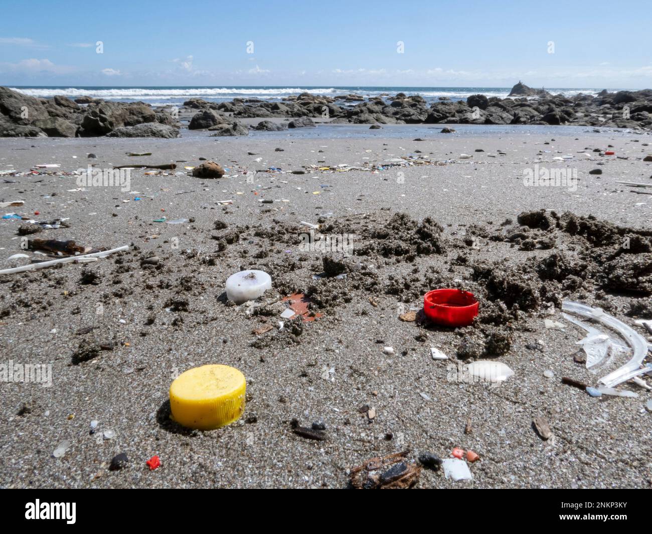 Tre tappi di plastica per bottiglie e altra plastica lavati su una spiaggia vicino Montezuma in Costa Rica Foto Stock