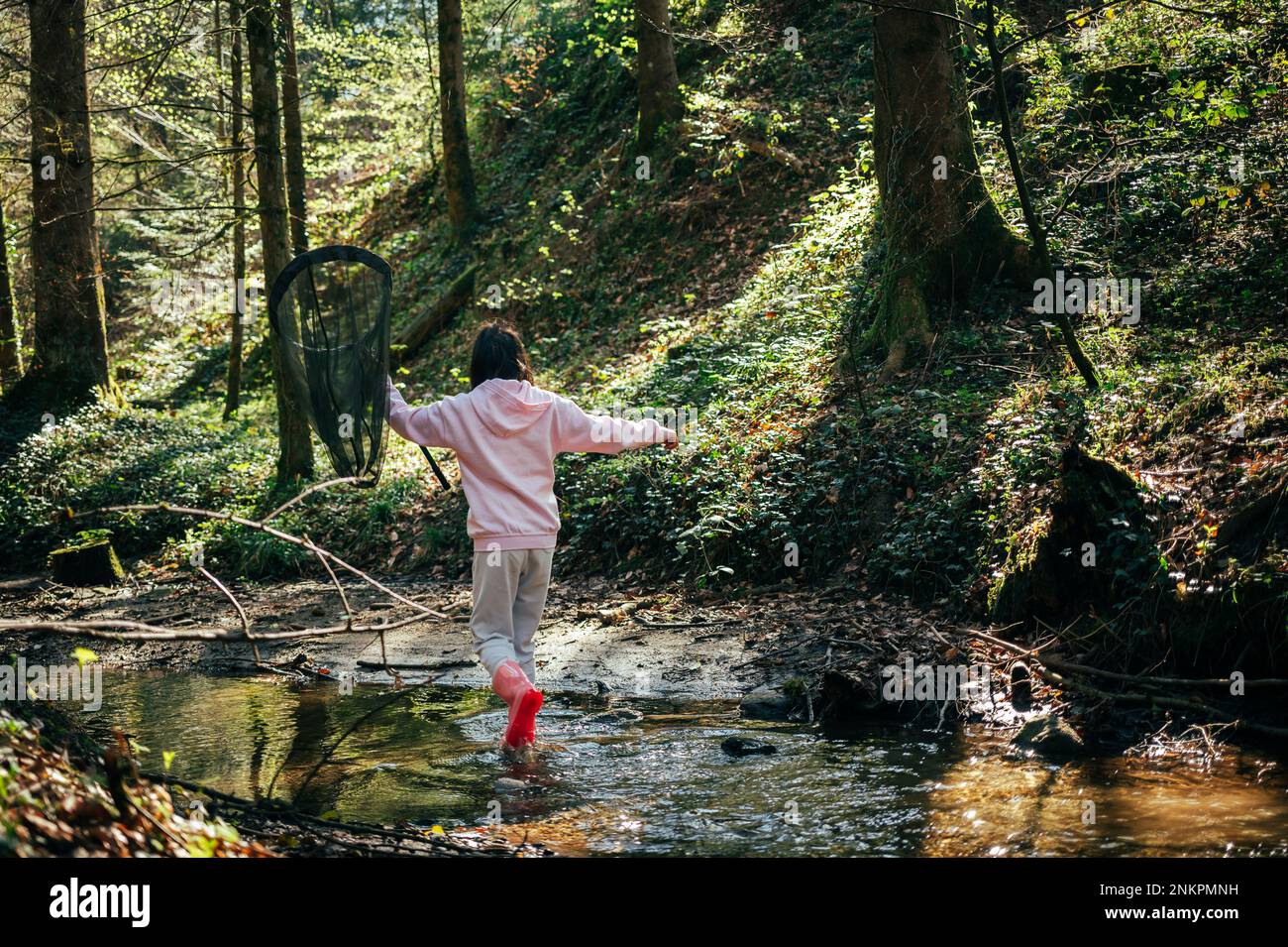 Persona nella foresta. Pesca infantile asiatica con una rete per scoprire la natura. Una ragazza in rosa che gioca in un ruscello in primavera. Foto Stock