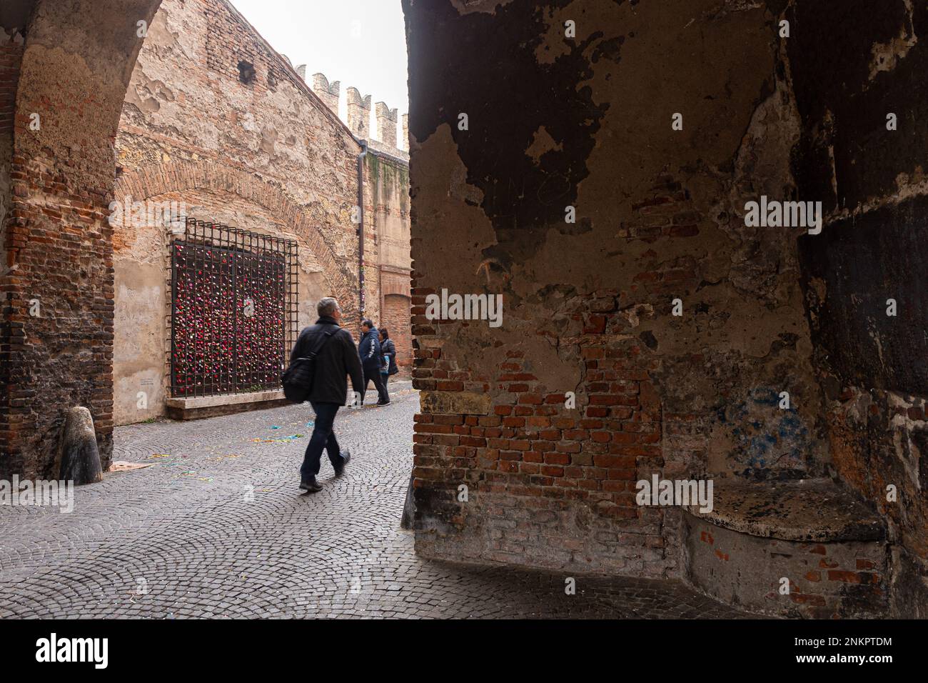 Persone che camminano attraverso un arco a Castelvecchio, Verona. Parete con lucchetti a forma di amore visibili. Foto Stock