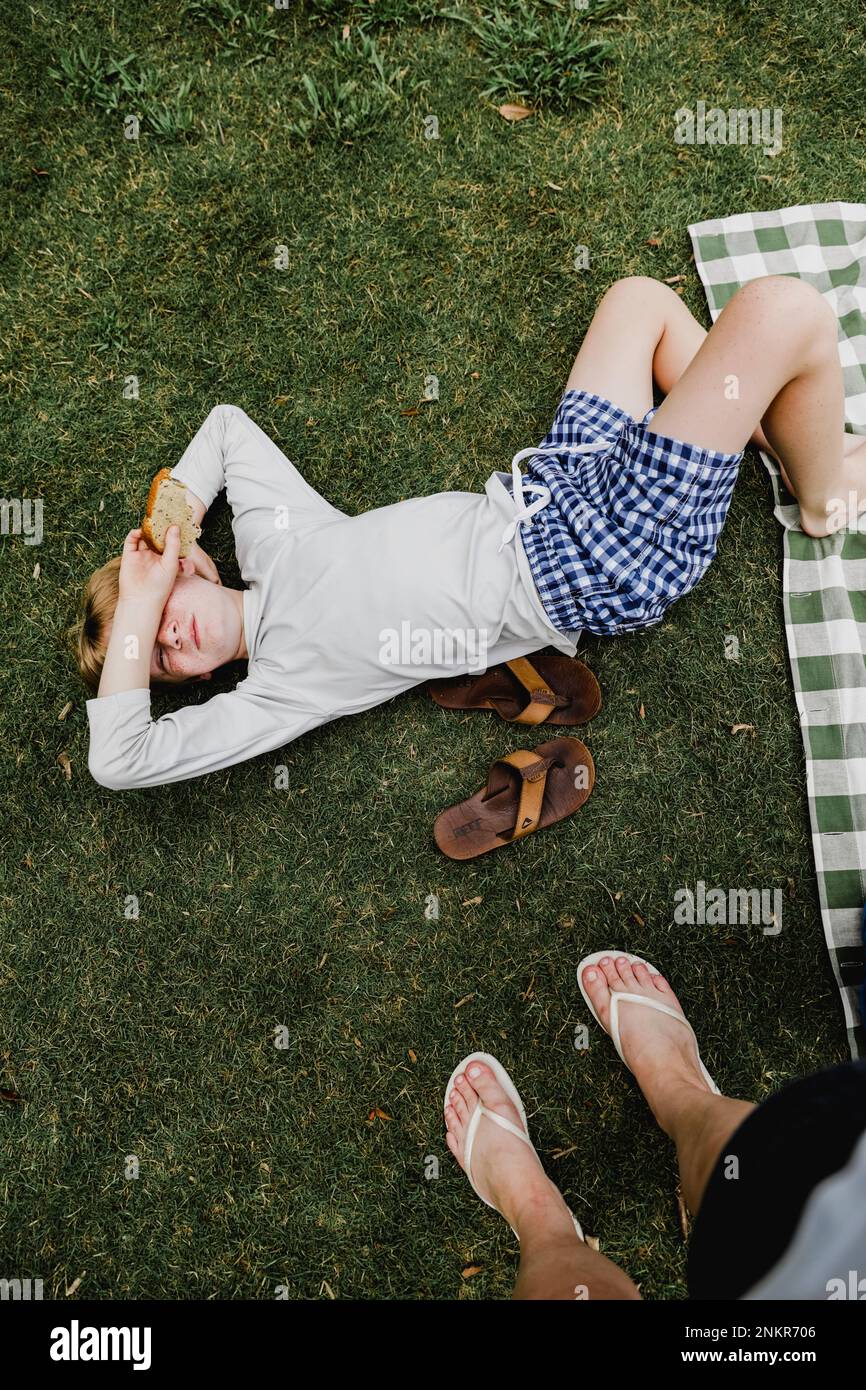 Ragazzo sdraiato sull'erba coprendo gli occhi con il braccio, la prospettiva personale Foto Stock