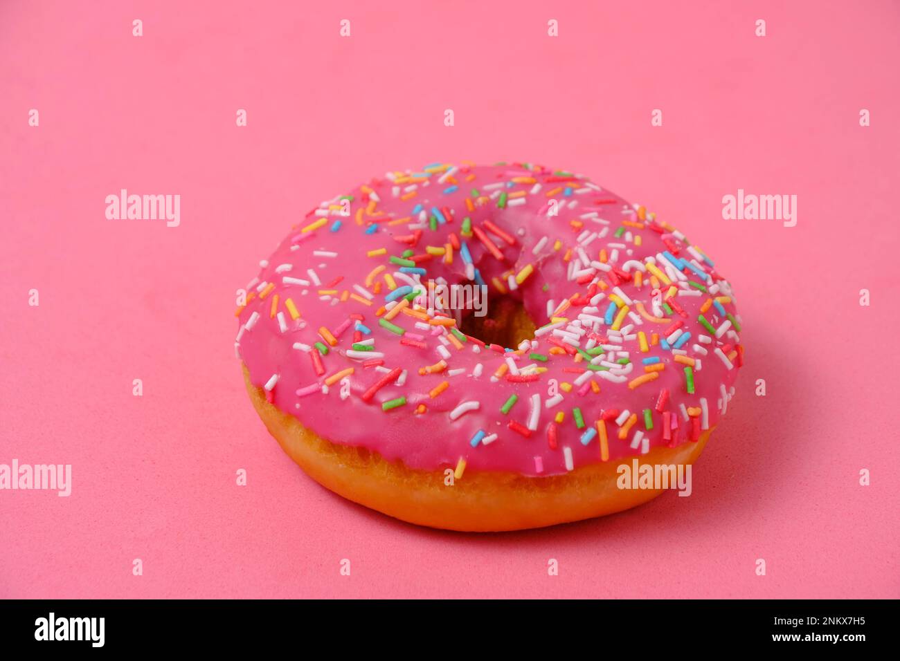 Ciambella con glassa rosa e zucchero multicolore spasles.on sfondo rosa Foto Stock