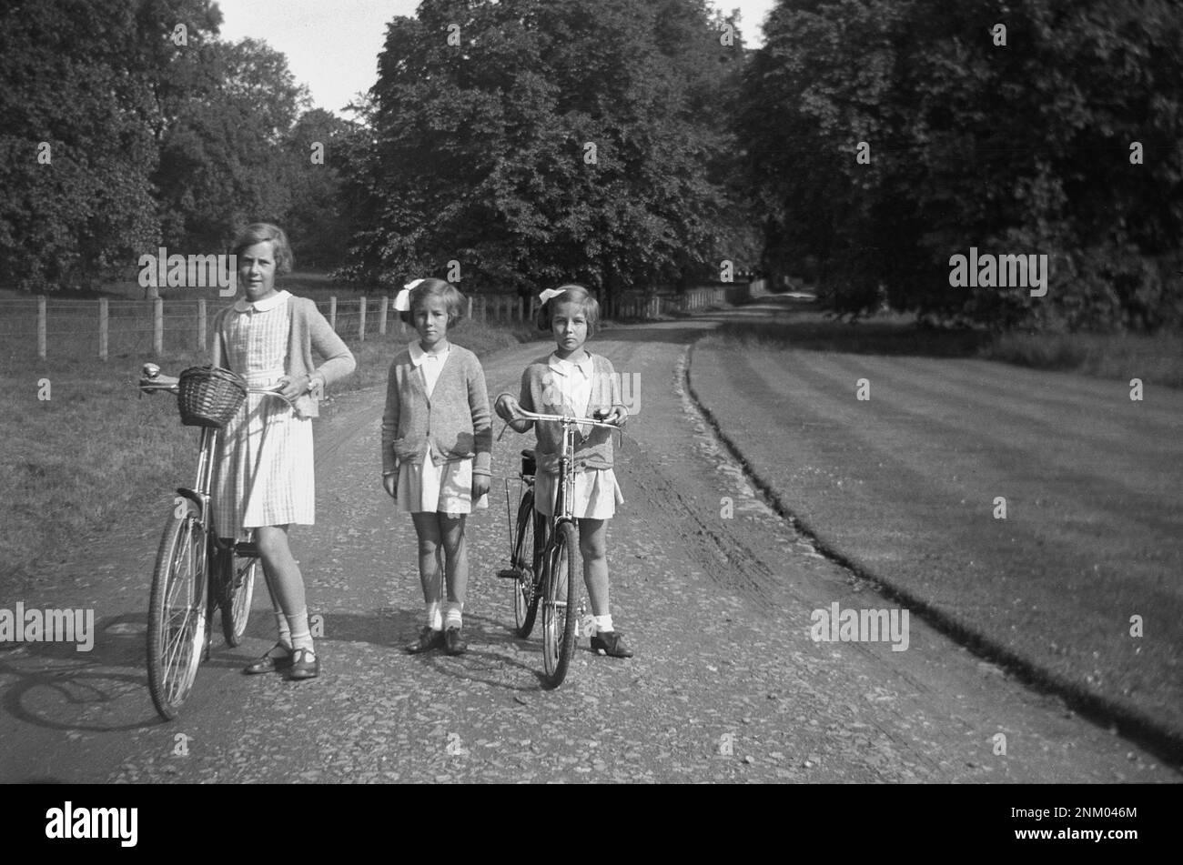 1934, storico, tornando a casa dalla scuola, tre giovani studentesse, due con le loro biciclette, fuori su un sentiero di ghiaia di una tenuta di campagna, Inghilterra, Regno Unito. Foto Stock