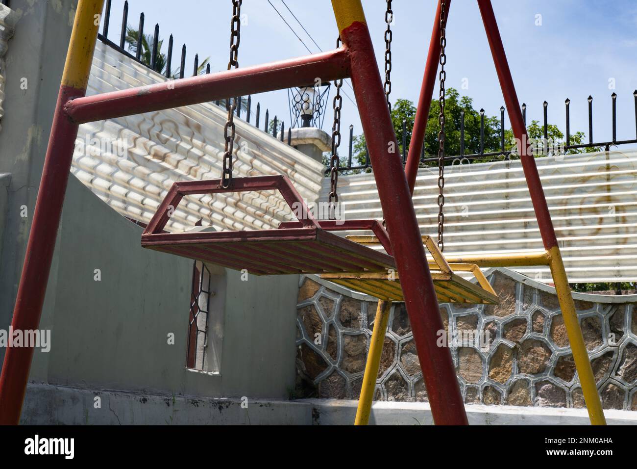 Altalena per bambini vecchi e arrugginiti. Verniciato di colore rosso e giallo. Parco giochi per bambini. Foto Stock