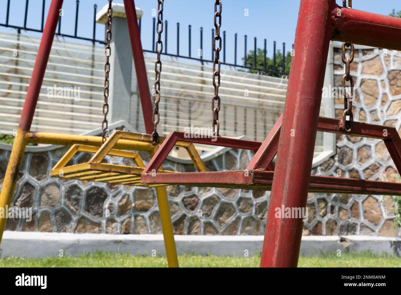 Altalena per bambini vecchi e arrugginiti. Verniciato di colore rosso e giallo. Parco giochi per bambini. Foto Stock