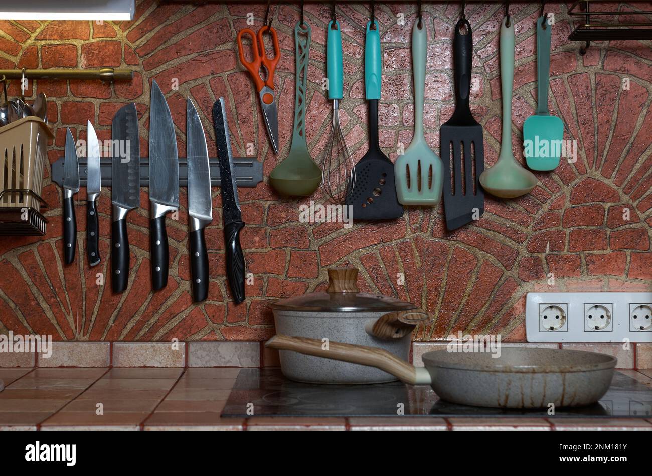 Parete della cucina decorata in mattoni con utensili da cucina appesi su di essa Foto Stock