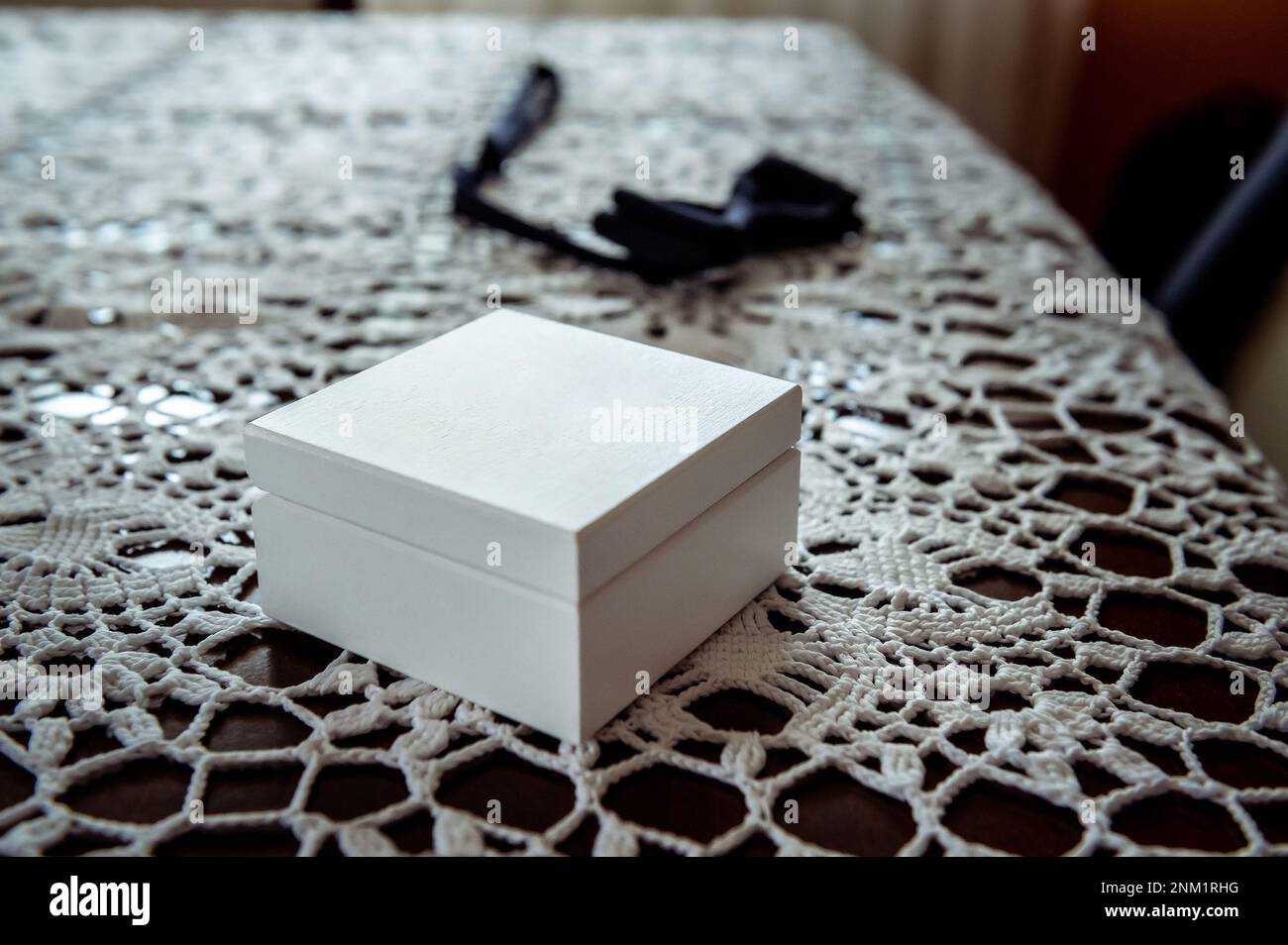 anelli di nozze e dettagli una scatola di legno bianco per anelli sdraiati su un tavolo con una tovaglia in pizzo con cravatta ad arco sullo sfondo Foto Stock