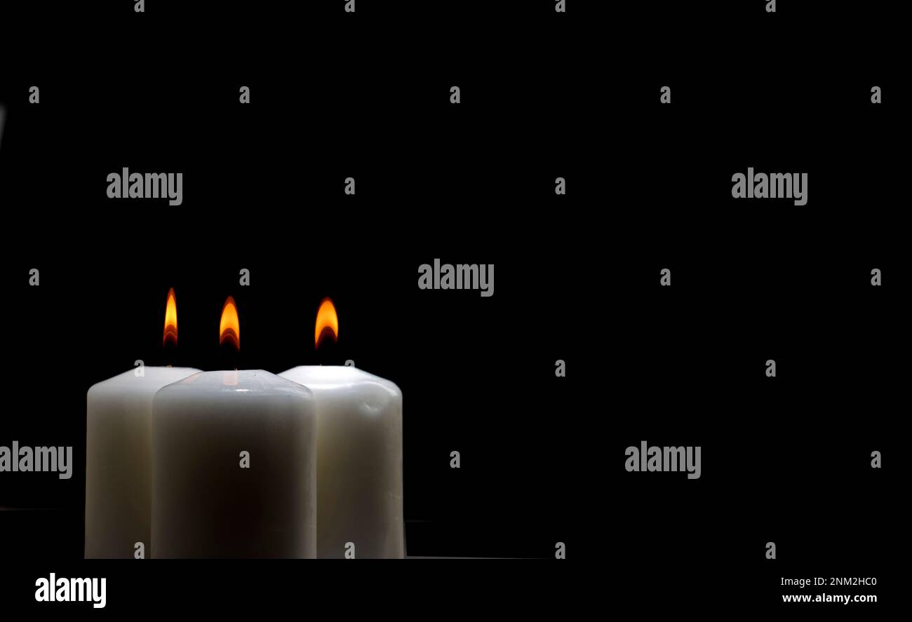 tre candele accese su un tavolo bianco con sfondo nero, spazio per il testo Foto Stock
