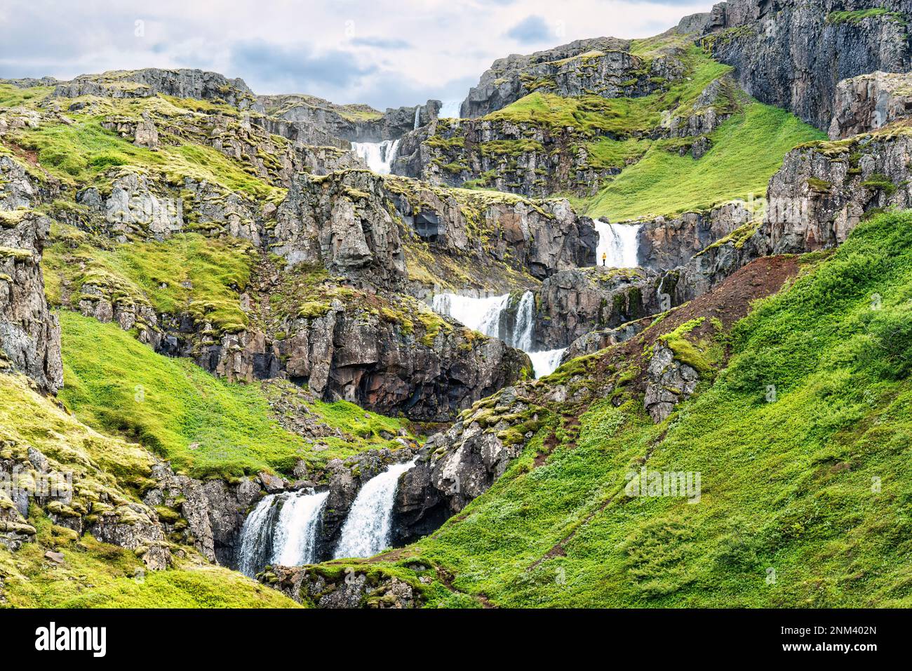 Vista maestosa della cascata a più livelli di Klifbrekkufossar che scorre dalla scogliera tra il muschio verde nel fiordo di Mjoifjordur in estate in Islanda Foto Stock