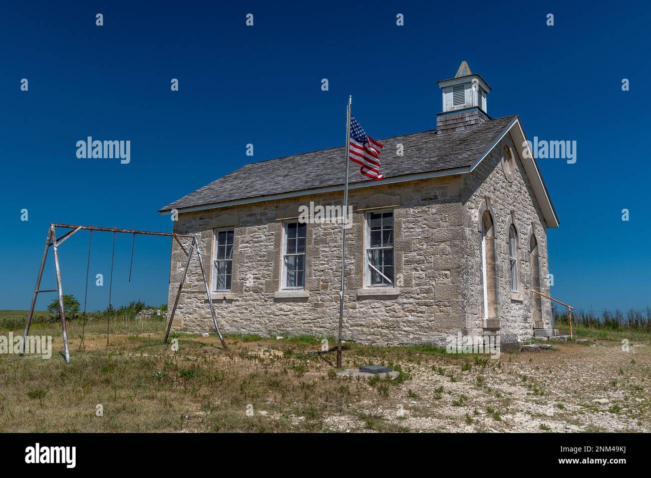 Una bella vecchia scuola storica con bandiera e playset ancora in piedi in alto sulla prateria del Kansas. Foto Stock