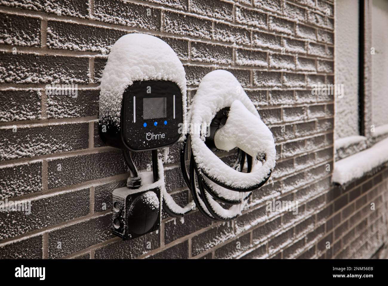 Punto di ricarica per auto elettriche all'esterno di una casa moderna nella neve Foto Stock