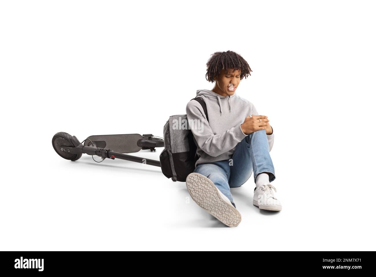 Ragazzo afro-americano seduto sul pavimento accanto a uno scooter elettrico e tenendo il ginocchio ferito isolato su sfondo bianco Foto Stock