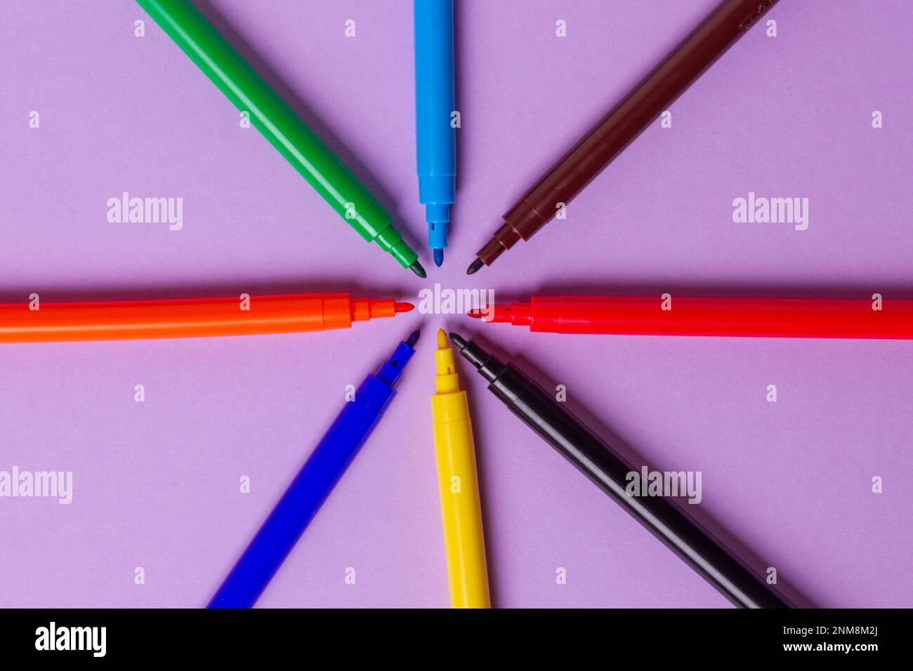 Pennarelli senza cappucci di colori diversi su sfondo viola. Disposti in cerchio. Foto Stock