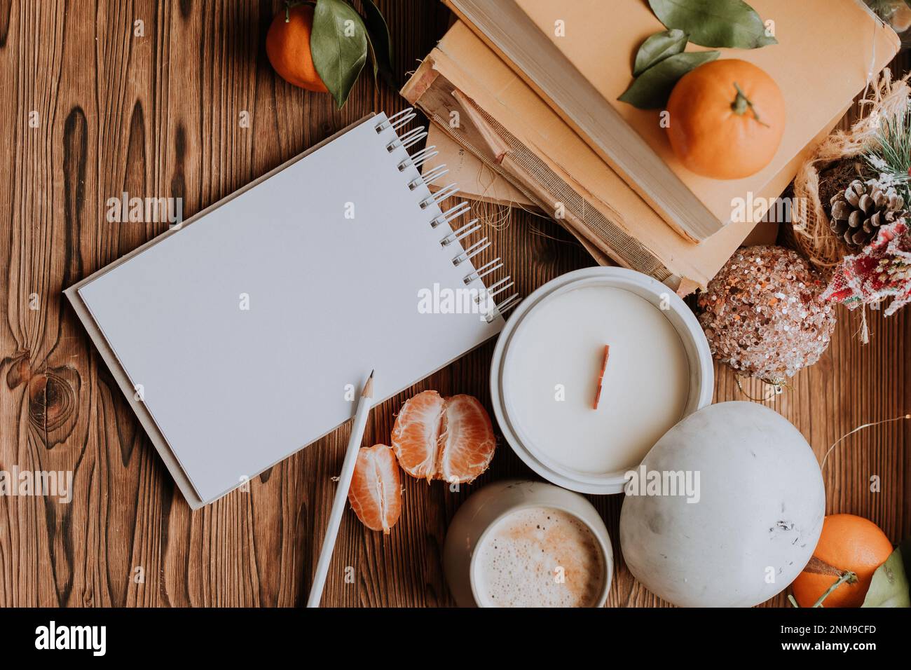 un notebook con pagine bianche accanto a libri e tangerini, candele fatte a mano. Piani e sogni per il nuovo anno Foto Stock