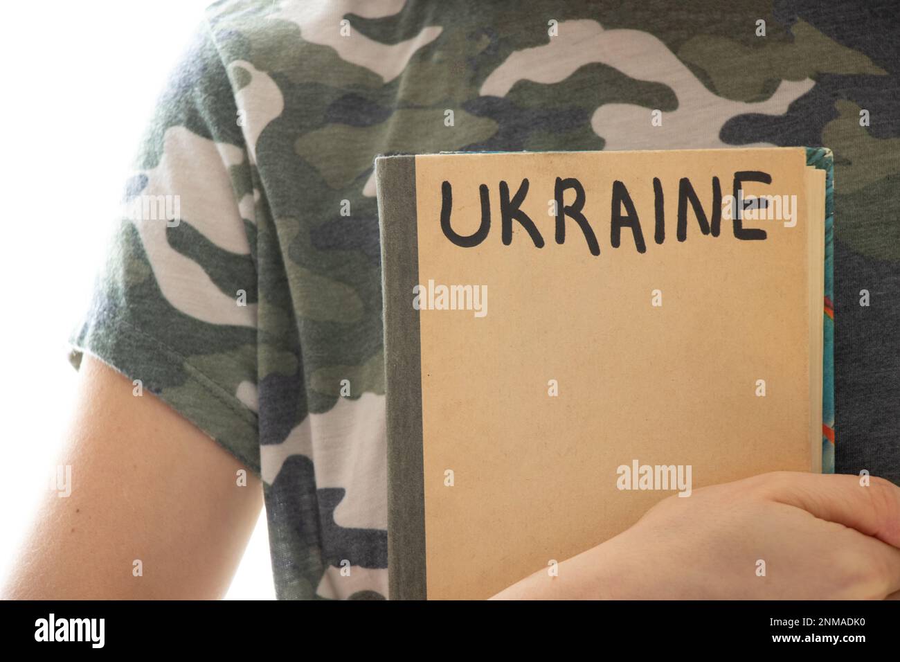 Una ragazza in uniforme mimetizzata con un libro su cui è scritta l'Ucraina, l'istruzione in Ucraina durante la guerra, studente Foto Stock