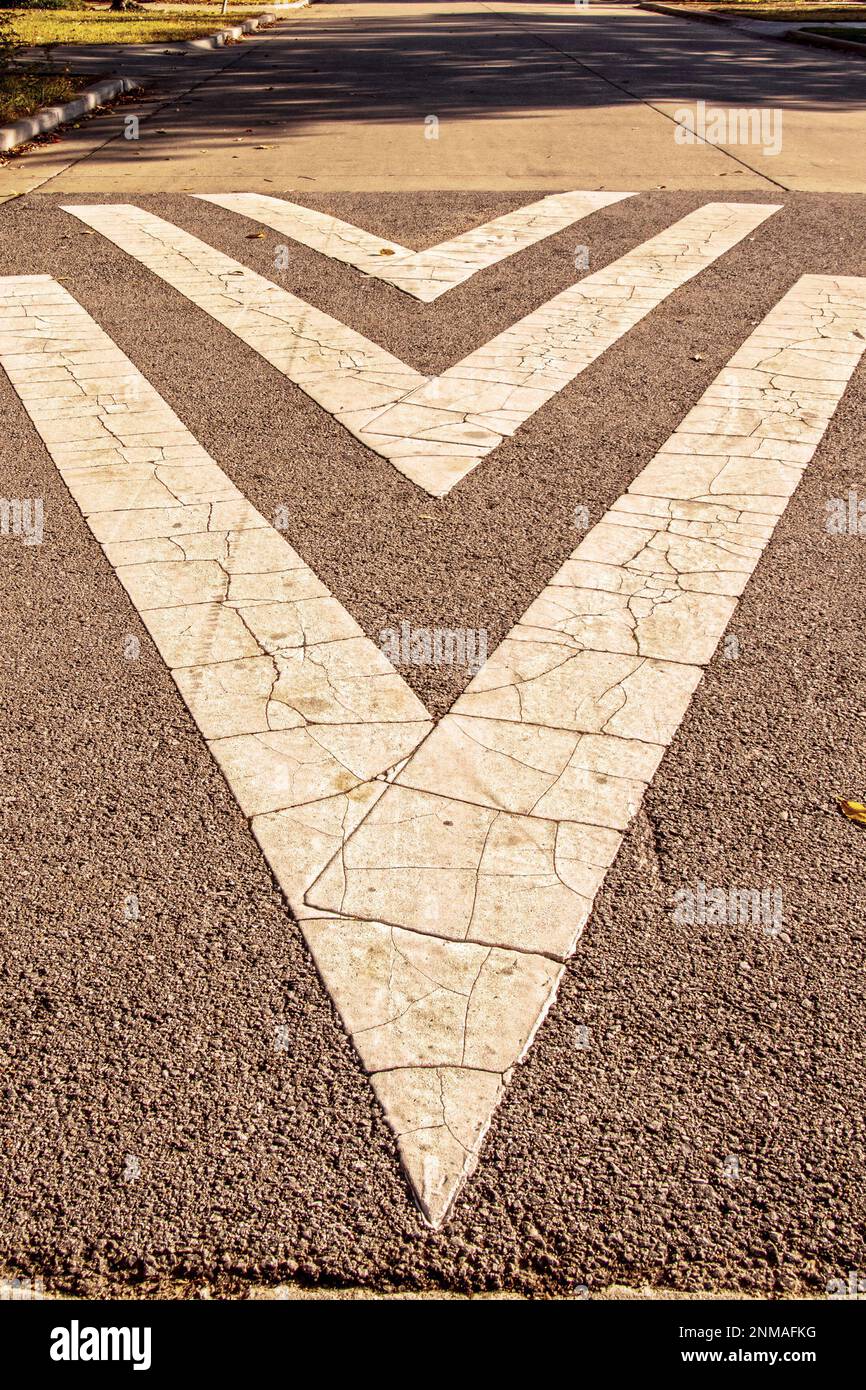 Frecce direzionali screpolate e grunghe dipinte su strade residenziali - asfalto molto strutturato con pavimentazione regolare con ombre d'albero in lontananza Foto Stock