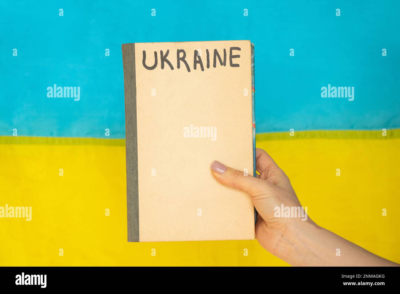La mano di una donna tiene un libro su cui l'Ucraina è scritta sullo sfondo della bandiera dell'Ucraina, l'istruzione in Ucraina durante Foto Stock