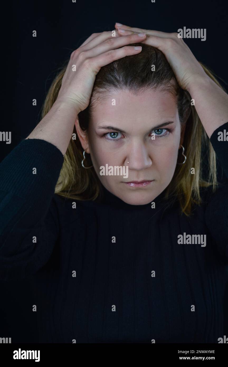 ritratto di una bella donna bionda che con le mani sulla testa ha uno sguardo molto determinato e decisivo Foto Stock