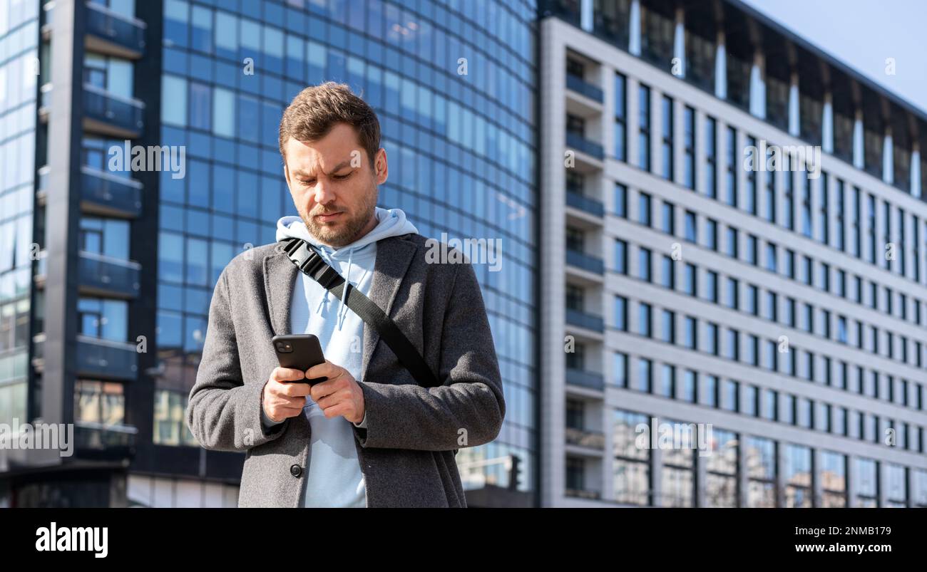 Uomo che utilizza il suo telefono cellulare on-line messaggistica in piedi per strada contro edificio urbano. Foto Stock