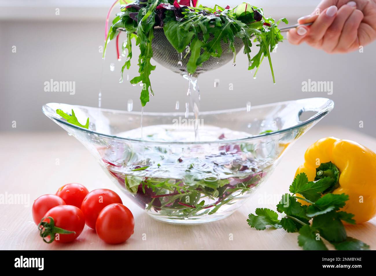 Una cuoco della donna in un grembiule striato sta strappando le foglie appena lavate, fresche e pulite di lattuga in una ciotola di vetro separata. Si trova in una cucina in stile rustico. Foto di alta qualità Foto Stock